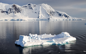 Холодный айсберг в воде у заснеженных гор, Антарктика