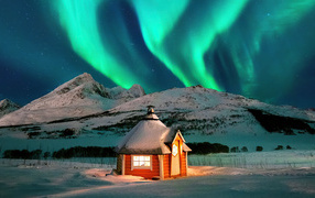 Green aurora over a house in the snowy mountains