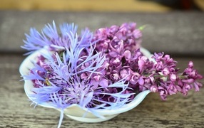 Цветы сирени и василька в вазе на столе