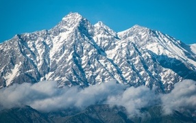 High snow-capped mountains in fog under blue sky