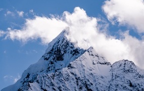 Острая заснеженная вершина горы в белых облаках