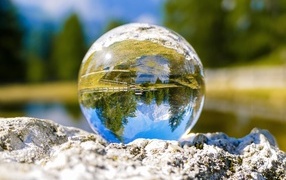 A glass ball stands on a stone near the water