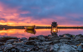 A kerosene lamp stands on stones by the lake