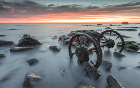 Old wheels lie in the water with stones