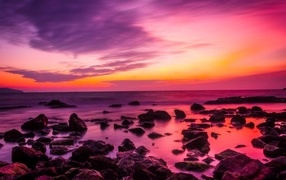 Розовый закат на каменном берегу моря