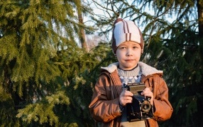 Мальчик с фотоаппаратом стоит у ели