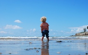 A little boy walks on wet sand by the sea