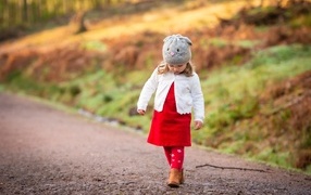 Маленькая девочка в красном платье гуляет по дороге