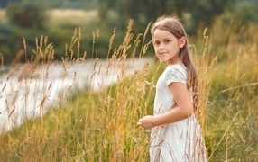 Маленькая девочка в белом платье гуляет по высокой траве