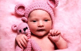 Грудной ребенок в розовой шапке с игрушкой в руке