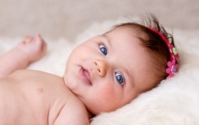 Blue-eyed newborn baby with a flower on her head
