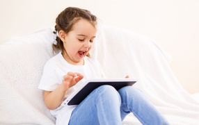 Веселая девочка с планшетом на кровати 