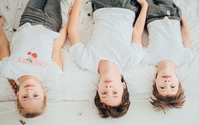 Дети в белых футболках лежат на кровати