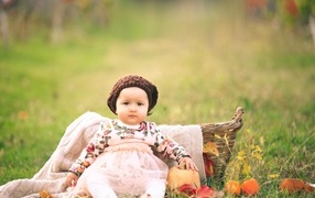 Милая маленькая девочка в шапке сидит на траве 