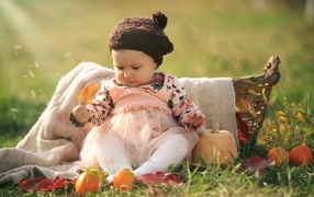 Funny little girl sits on the grass with a pumpkin