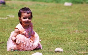Девочка в розовом платье играет на зеленой траве