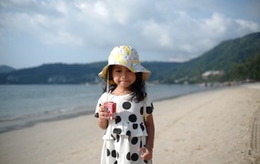 Девочка с соком в руках стоит на пляже