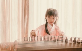 Маленькая девочка азиатка играет на музыкальном инструменте