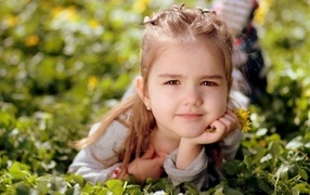 Маленькая кареглазая девочка лежит на траве с цветами