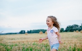 Little cheerful girl runs across the field