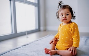 Маленькая смешная девочка сидит у окна