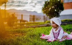 Маленькая девочка в розовом платье сидит на траве