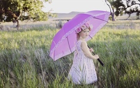 Little girl stands in the grass with an umbrella