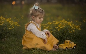 Маленькая девочка с игрушечной машиной сидит на траве