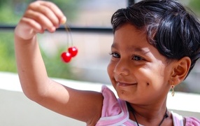 Маленькая улыбающаяся девочка с ягодами вишни в руках