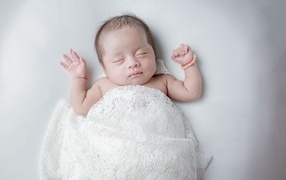 Маленький спящий ребенок на сером фоне под белым покрывалом