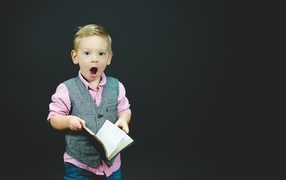 Удивленный мальчик с книгой в руках на черном фоне