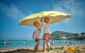 Two boys on the beach under an umbrella