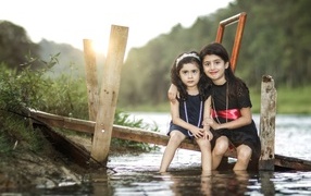 Две девочки сидят на мосту у реки