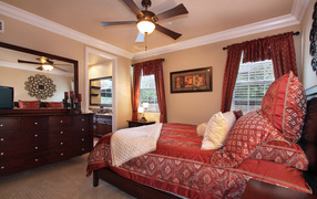 Много подушек на кровати с красным покрывалом в спальне