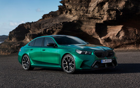 Зеленый автомобиль BMW M5 2024 года на фоне гор