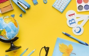 Красивые канцелярские предметы и глобус на желтом фоне