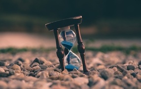 Песочные часы лежат на мелких камнях