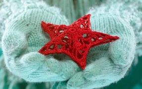 Красная вязаная звезда в руках в варежках