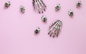 Кисти рук скелета и черепа на розовом фоне