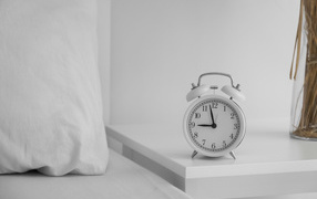 Будильник стоит на тумбочке у кровати 