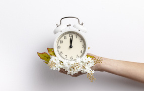 Белый будильник в руке с цветами на сером фоне