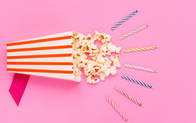 Коробка попкорна со свечами на розовом фоне