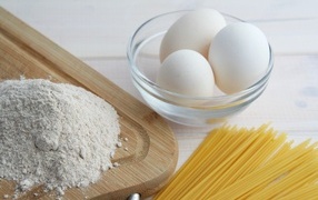 Яйца на столе с мукой и спагетти