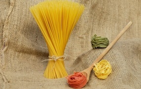 Разноцветные макаронные изделия с деревянной ложкой на мешке