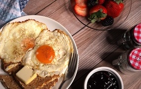 Яичница с гренками на столе с клубникой