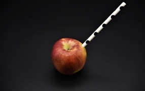 Большое красное яблоко с трубочкой на черном фоне