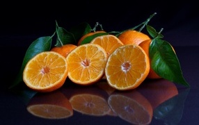 Половинки мандарина с листьями на черной поверхности