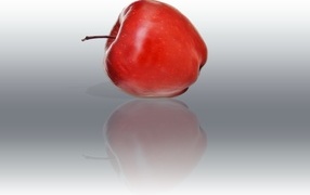 Красное яблоко отражается в серой поверхности