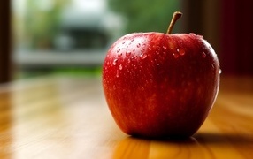 Красное яблоко в каплях воды на столе