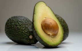 Спелое зеленое авокадо с косточкой на сером фоне